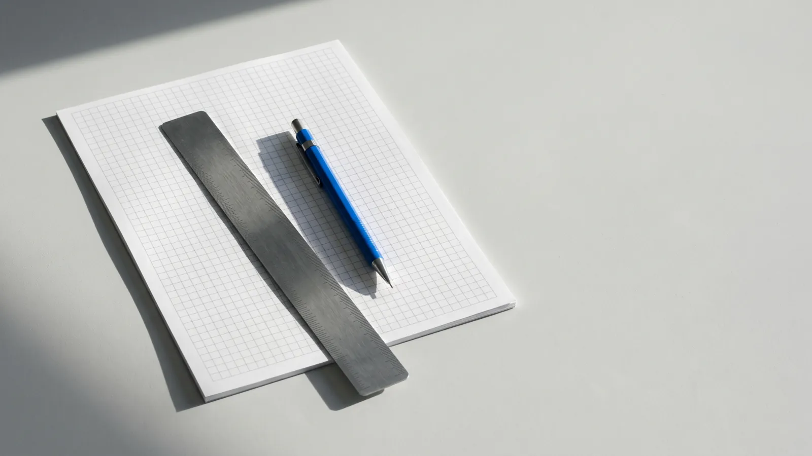 Blank grid paper with a steel ruler and a blue mechanical pencil.