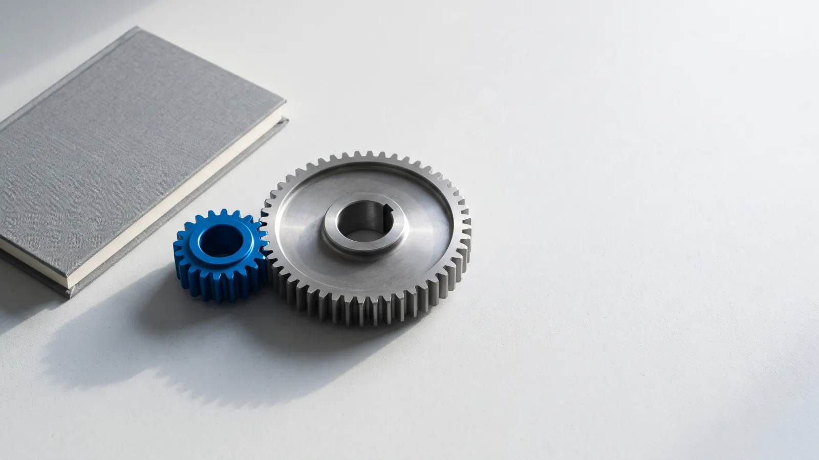 Two meshing steel gears beside a closed ledger, the smaller gear blue.